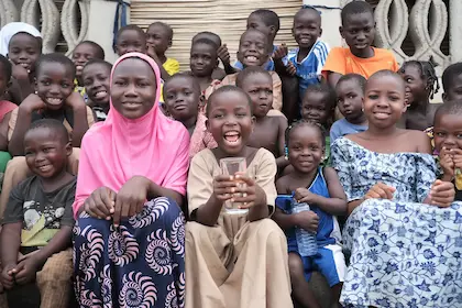 Un groupe d'enfants assis et souriants, certains tenant des bouteilles ou des verres d'eau